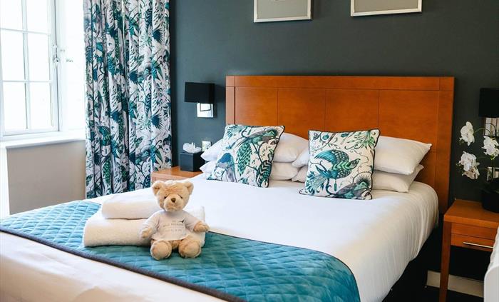 Hotel bedroom at Wild Pheasant Hotel & Spa featuring a neatly made bed with folded towels, illuminated by natural daylight coming through the window.